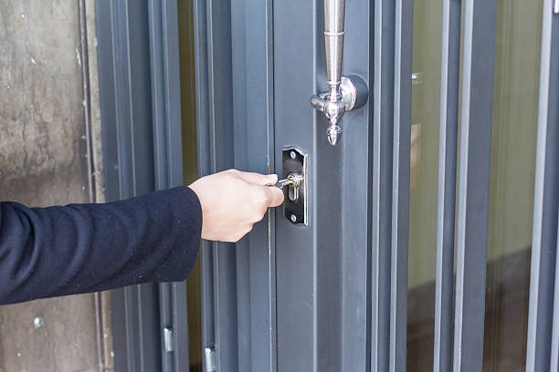 Person unlocking a modern glass door with a silver key. -emergency locksmith services